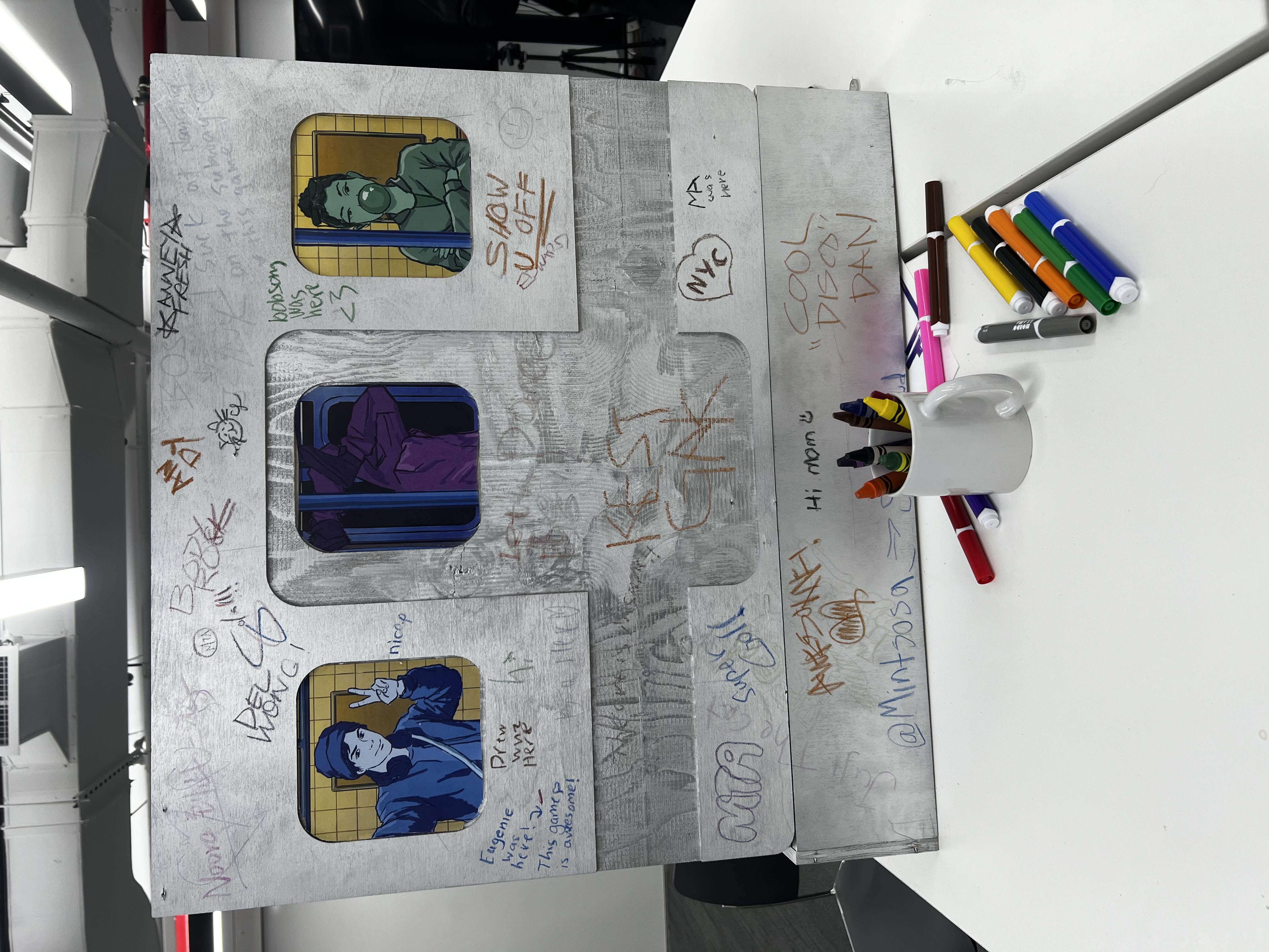 Other side of the cabinet showing vinyl character windows surrounded by marker and crayon tags, with crayons and markers sitting nearby